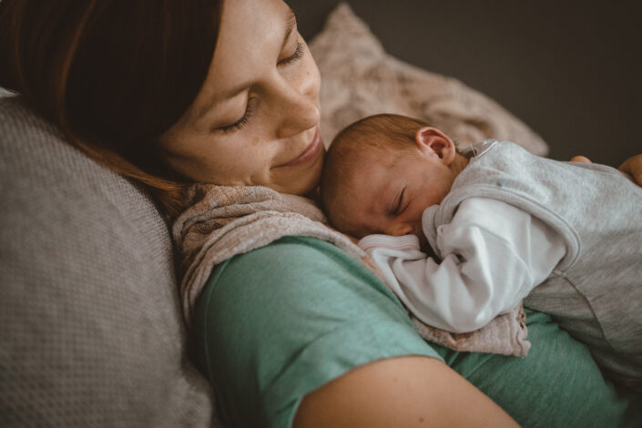 Mutter blickt liebevoll auf Neugeborenes das auf ihrer Brust schläft