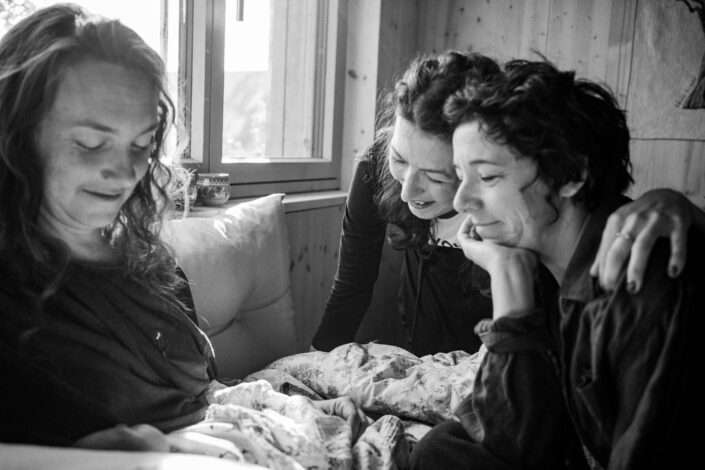 Doula bestaunt mit zwei Mamas das Baby beim Fotoshooting im Wochenbett