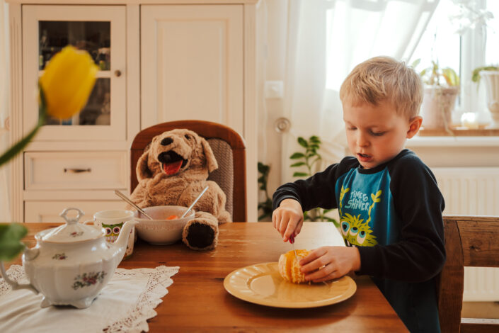 Junge sitzt mit Stofftier beim Frühstück beim Familienshooting