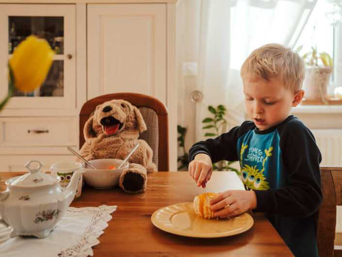 Junge sitzt mit Stofftier beim Frühstück beim Familienshooting