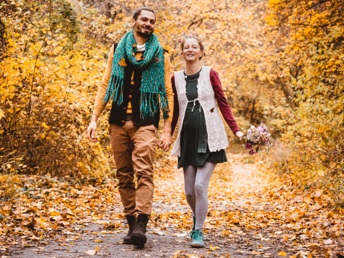 Man und Frau mit Babybauch spazieren durch Herbst bei dokumentarischen Familienfotoshooting