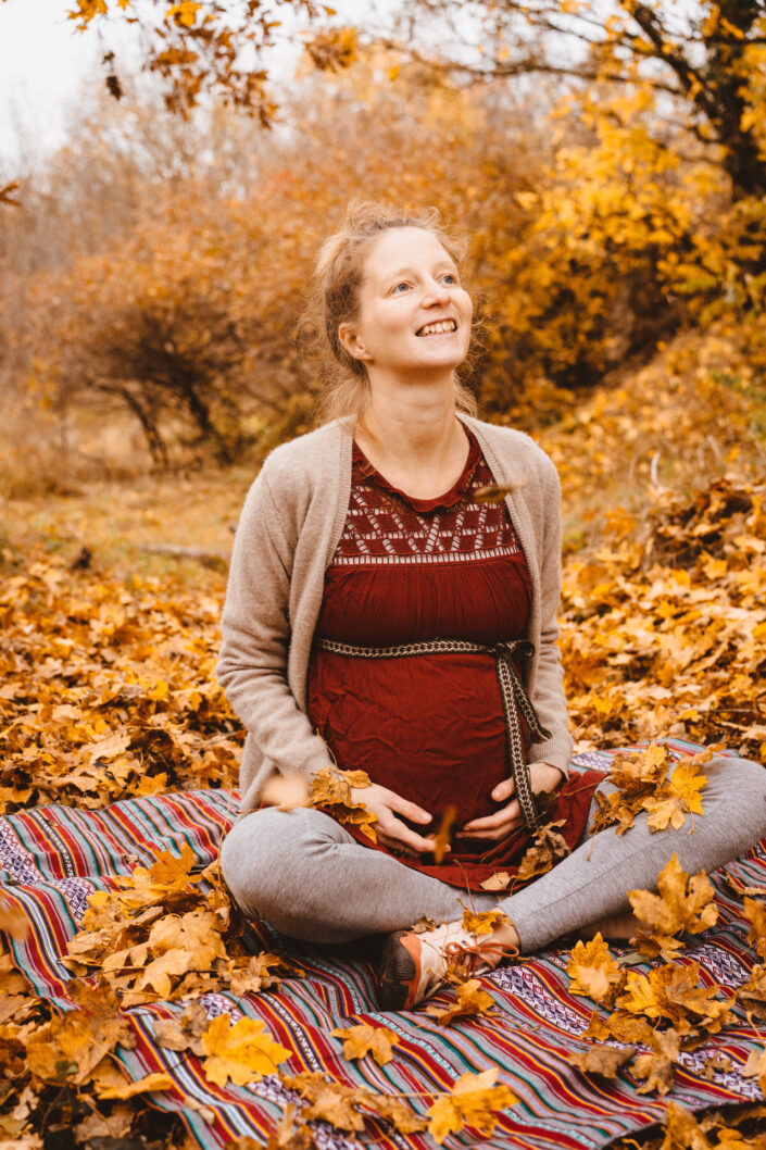 Herbstbild von Frau mit Babybauch sitzend in der Natur, dokumentarische Familienfotografie