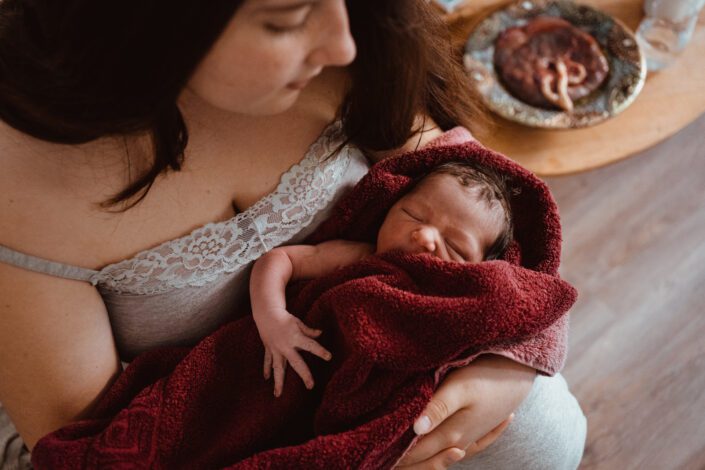 Frischgeborenes Baby im Arm mit Plazenta bei Geburtsfotografie