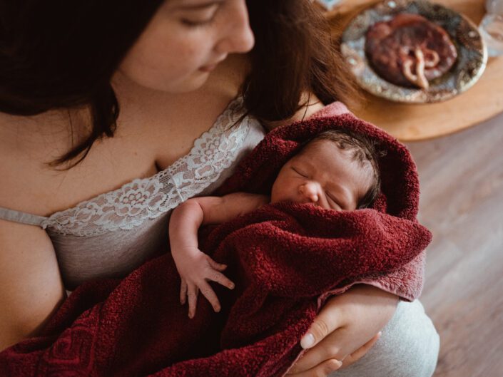 Frischgeborenes Baby im Arm mit Plazenta bei Geburtsfotografie