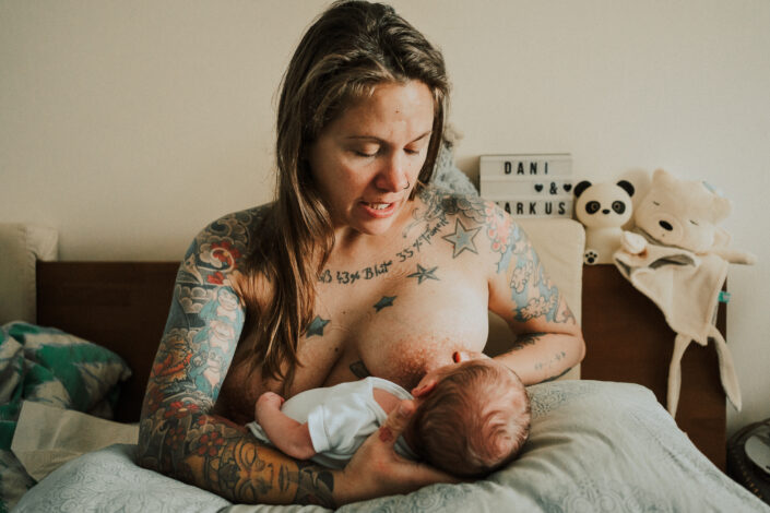 Mutter stillt Neugeborenes im Bett beim Wochenbettshooting