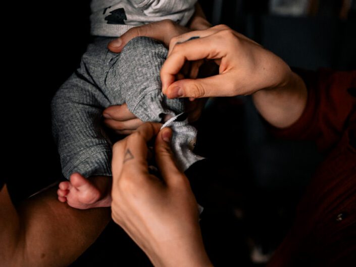 zwei Hände ziehen dem neugeborenen Baby die graue Hose an