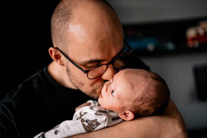Vater küsst Baby im Wochenbett
