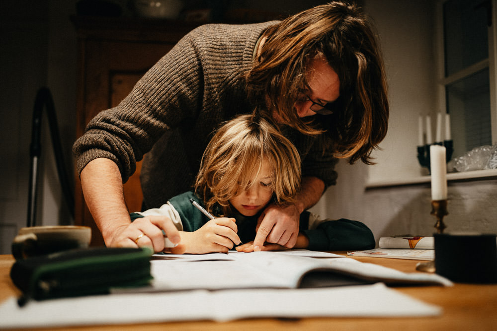Vater lernt mit Kind und beugt sich über die Hausaufgaben