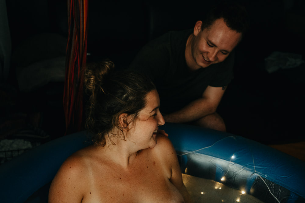 Mutter lacht im Geburtspool bei Hausgeburt