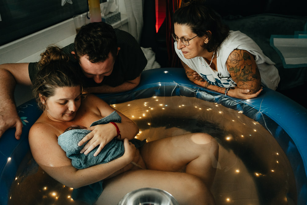 Eltern bestaunen Baby nach Geburt im Pool mit Hebamme - Geburtsfotografie