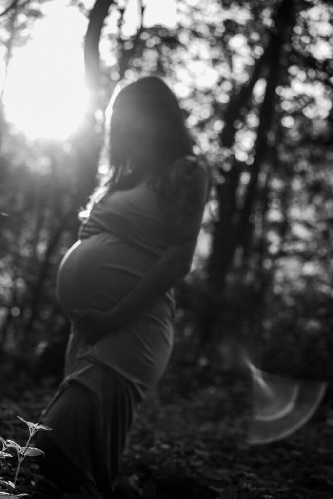 schwarz weißes Babybauchbild mit Kleid im Wald bei Gegenlicht - natürliche Schwangerschaftsfotografie