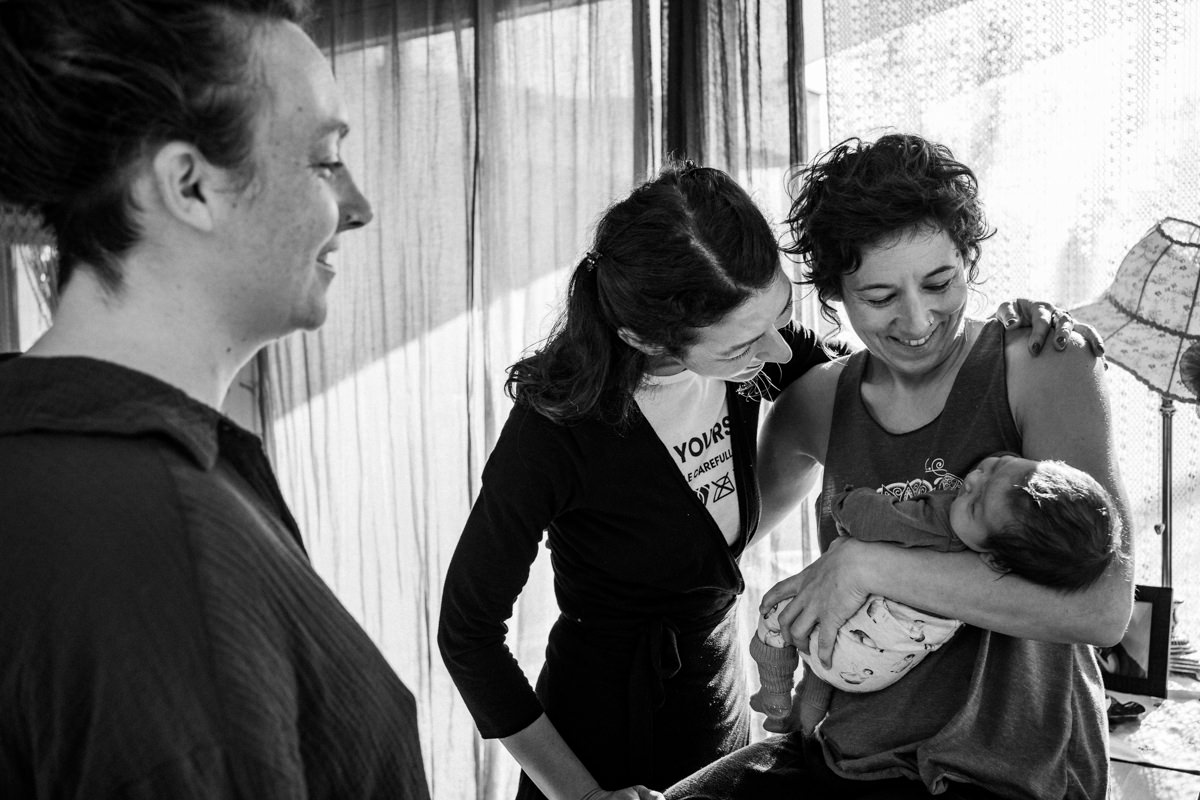 Neugeborenes liegt im Arm seiner Mama – Geburtsfotografie und Doula schaut liebevoll auf Baby