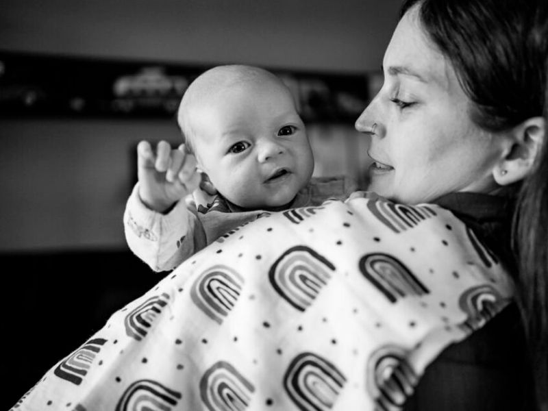 Frisch Geborenes Baby im Wochenbett schaut über die Schulter der Mutter