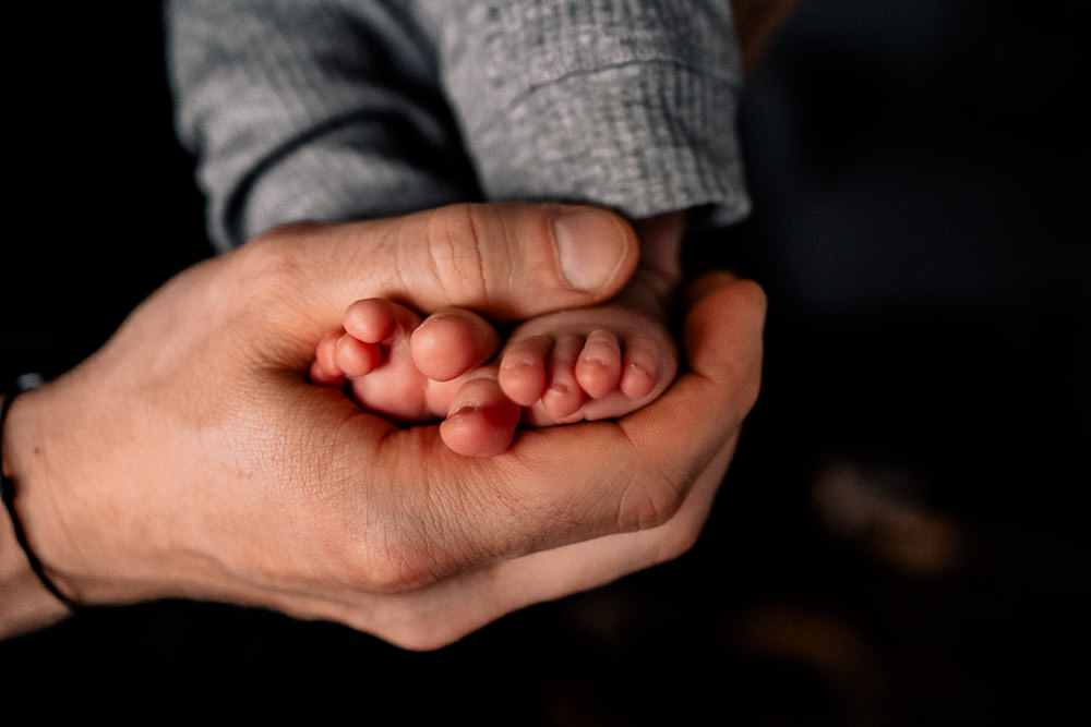 Fotobesuch im Wochenbett 8 Hände halten Füße von neugeborenem Baby