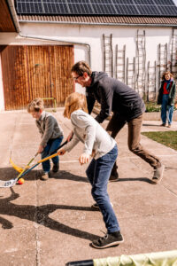 Kinder spielen Hockey mit Vater bei Familienshooting im eigenen Hof